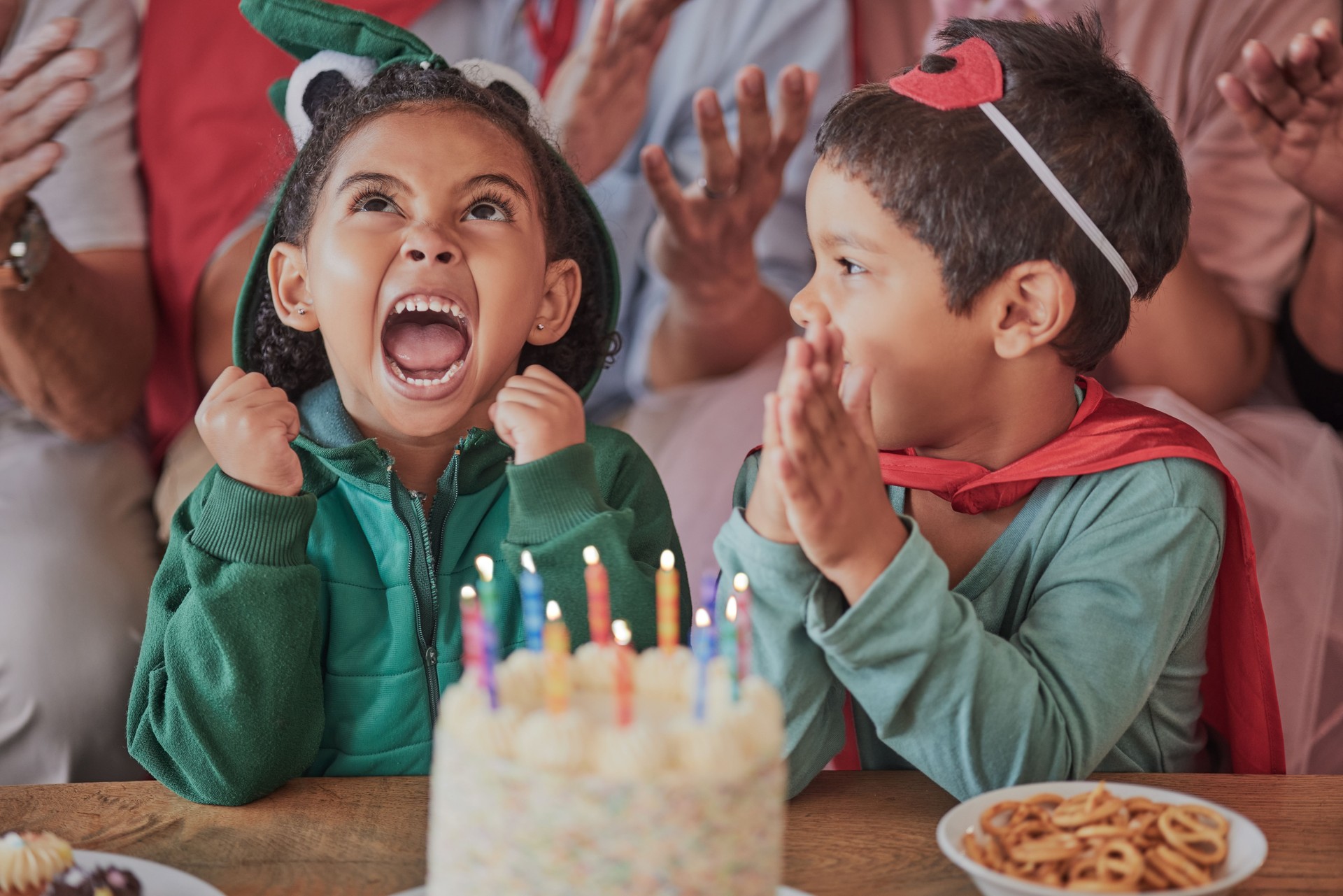 Happy birthday, party and children in halloween costume to celebrate young and fun girls special day together. Cake, fantasy and excited kid in a dinosaur monster outfit and boy in a superheroes cape